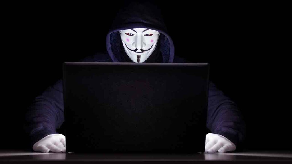 Pildil on arvuti ees olev maskiga häkker mis illustreerib teemat: Krüpto pettused kasutavad tuntud nimesid