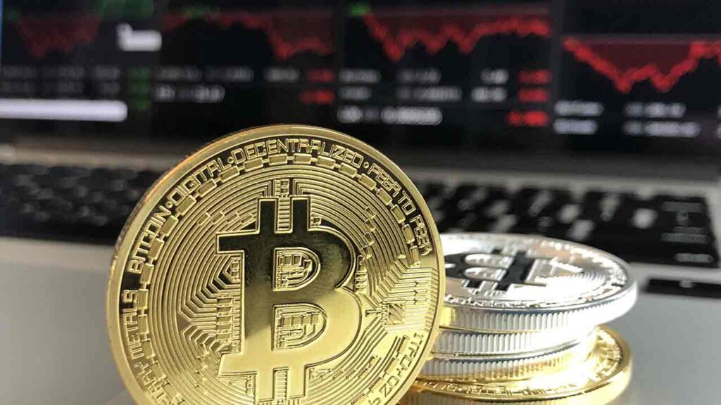 Pildil on aktsiagraafikud arvutiekraanil ning bitcoini münt, mis illustreerib teemat